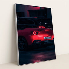 This photo shows a red Ferrari sports car driving at night, illuminated by neon lights, with a black Audi in the background, in a silver frame.