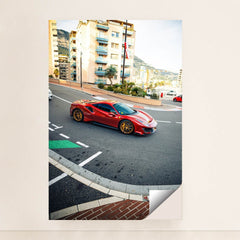 This photo shows a red Ferrari 488 Pista with gold wheels driving through a city street with Mediterranean buildings, unframed style.