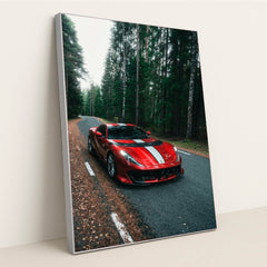 This photo shows a red Ferrari 812 Competizione with a white racing stripe parked on a winding forest road, in a silver frame.