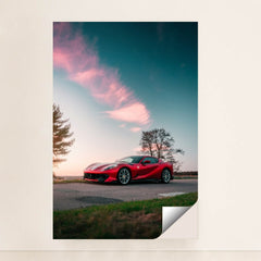 This photo shows a red Ferrari sports car parked on a rural road under a pink-clouded sunset sky, minimalist unframed style.