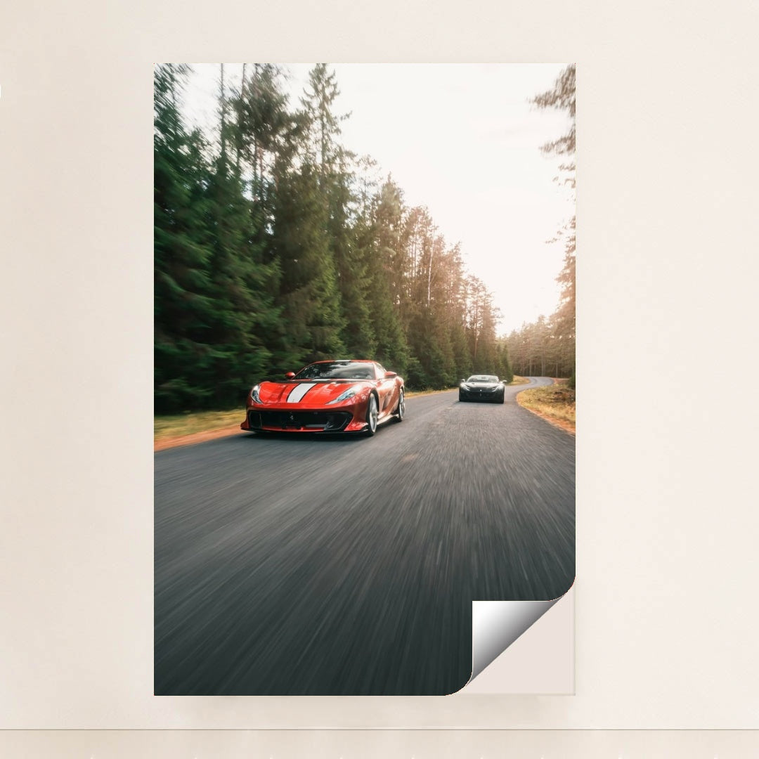 This photo shows a red Ferrari sports car with white stripes leading another car on a winding forest road, minimalist unframed style.