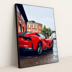 This photo shows the rear three-quarter view of a red Ferrari 812 Superfast parked on a wet city street, in a black frame.