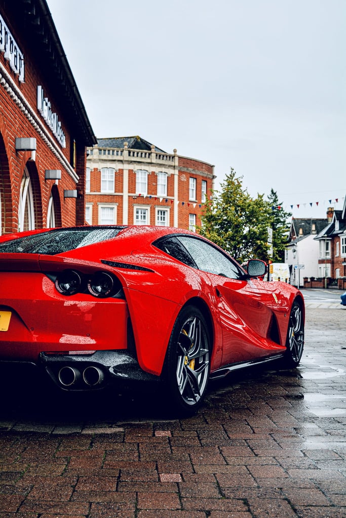 Ferrari 812 Superfast on Wet Streets, glossy red car reflecting on wet pavement in an urban setting.