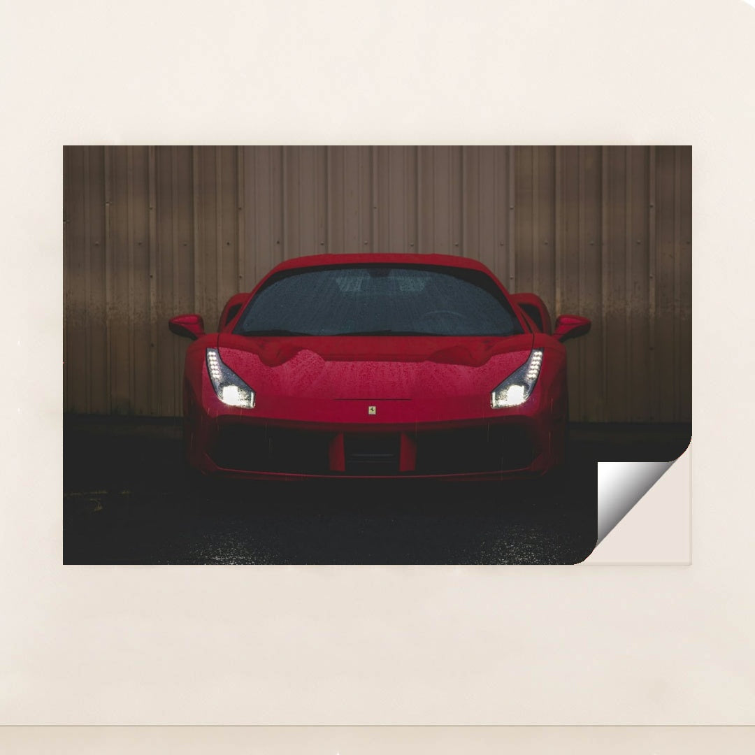 This photo shows the front view of a red Ferrari sports car with headlights on, parked on wet pavement near a metal wall, minimalist unframed style.