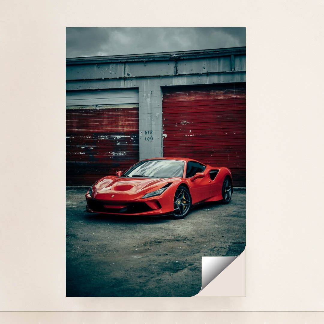 This photo shows a red Ferrari F8 Tributo parked in front of weathered red garage doors on a cloudy day, unframed style.