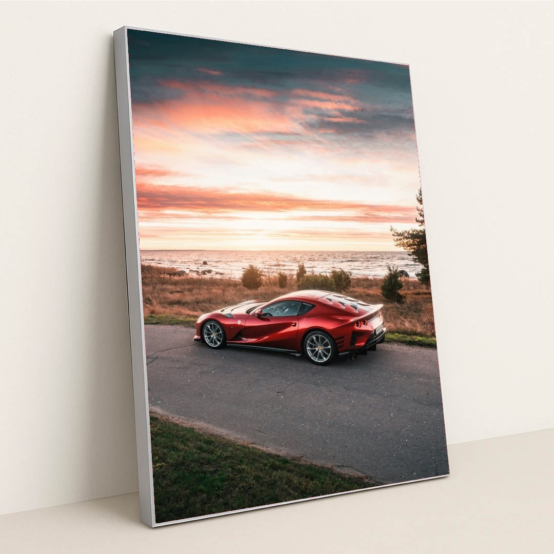 This photo shows a red Ferrari 812 Superfast parked by the seaside at sunset, in a silver frame.