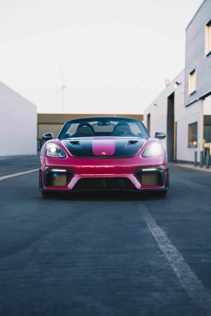 Magenta Porsche 718 Spyder parked on an urban street, showcasing its vibrant color and sleek design, perfect for car wall art.