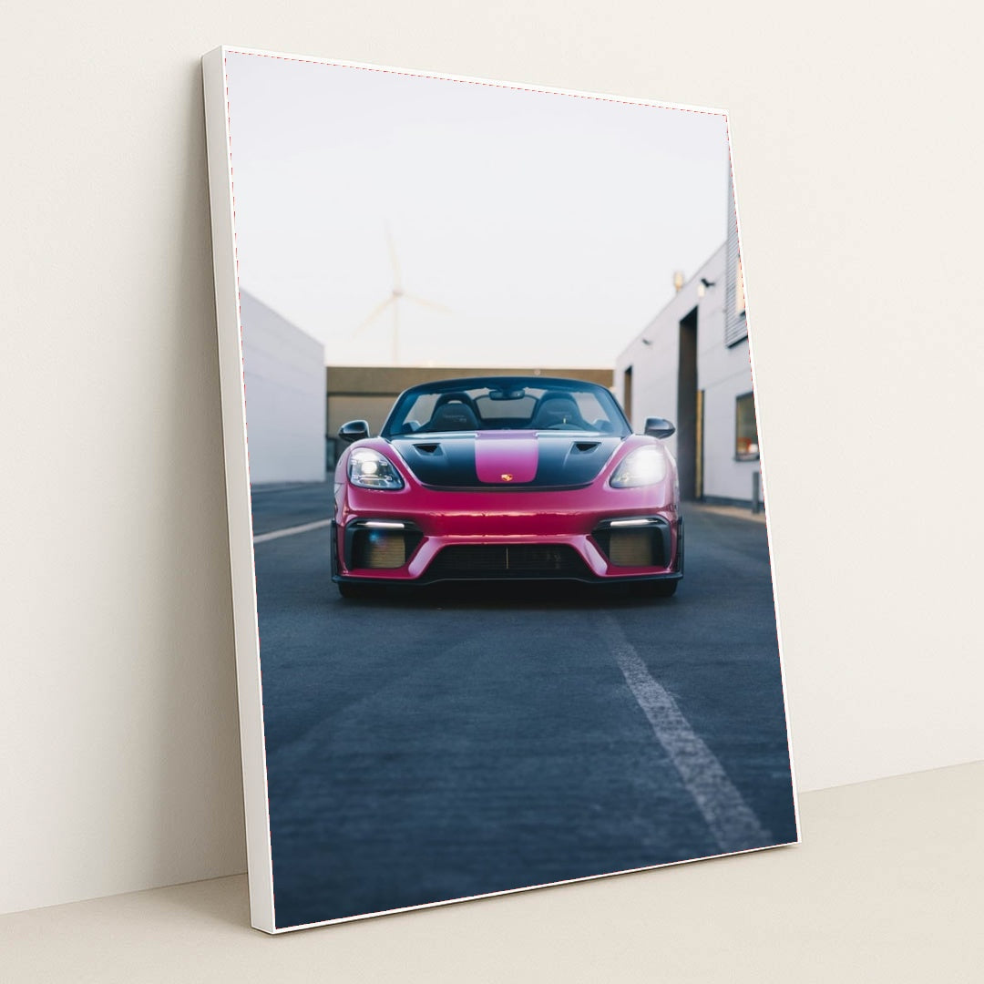 This photo shows a pink and black Porsche sports car viewed from the front, parked on an urban street, in a white frame.