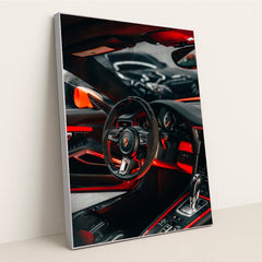 This photo shows the interior of a Porsche with a black and red steering wheel, paddle shifters, and orange accents, in a silver frame.