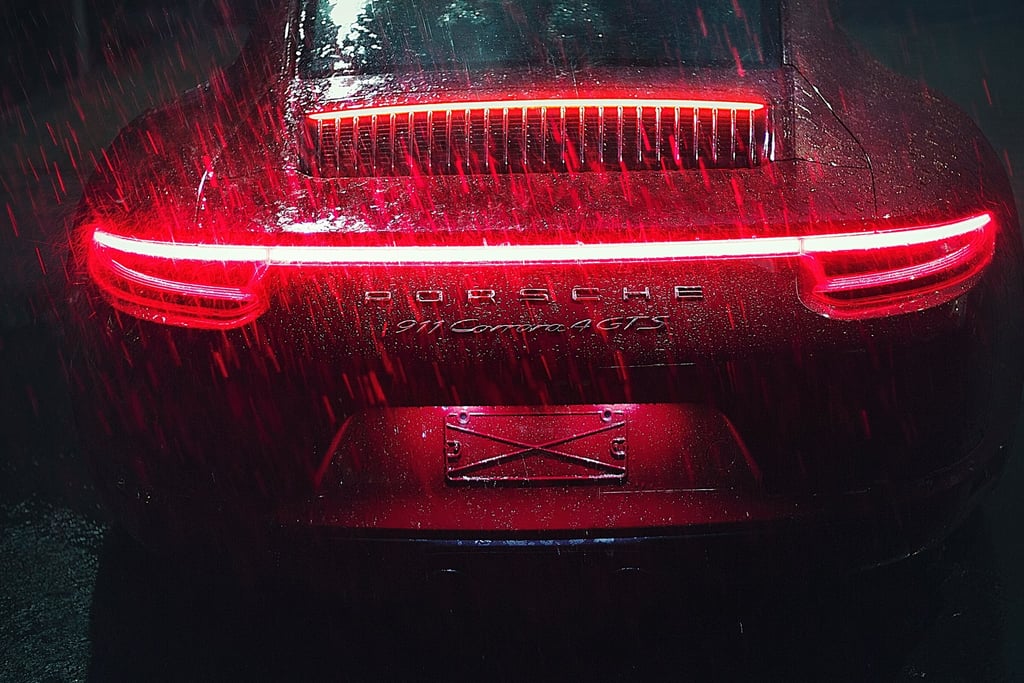 Crimson Porsche 911 in the Rain with gleaming LED taillights and raindrops creating a striking contrast on its body.