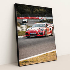 This photo shows a red Porsche GT3 RS race car with white stripes driving on a track during a motorsport event, in a black frame.