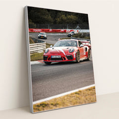 This photo shows a red Porsche GT3 RS race car with white stripes driving on a track during a motorsport event, in a silver frame.
