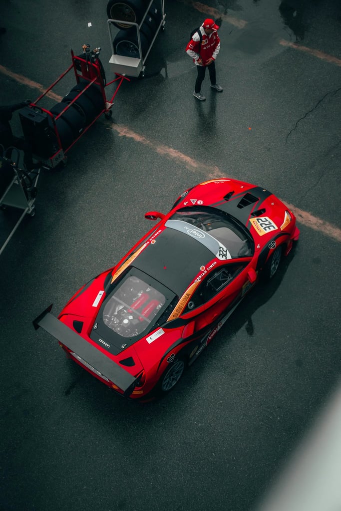 Ferrari GT in the Pits - aerial view of a vibrant red race car with a large rear wing on dark asphalt, highlighting its motorsport features.