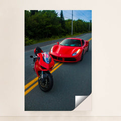 This photo shows a red Ducati motorcycle and a red Ferrari sports car parked side by side on a rural road, minimalist unframed style.