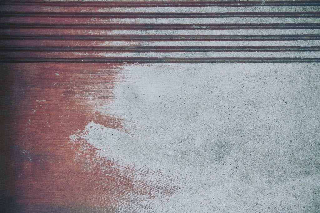 Tim Mossholder - A close-up view of a textured and stained concrete surface with a red hue and parallel lines.