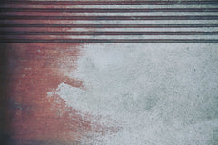 Tim Mossholder - A close-up view of a textured and stained concrete surface with a red hue and parallel lines.