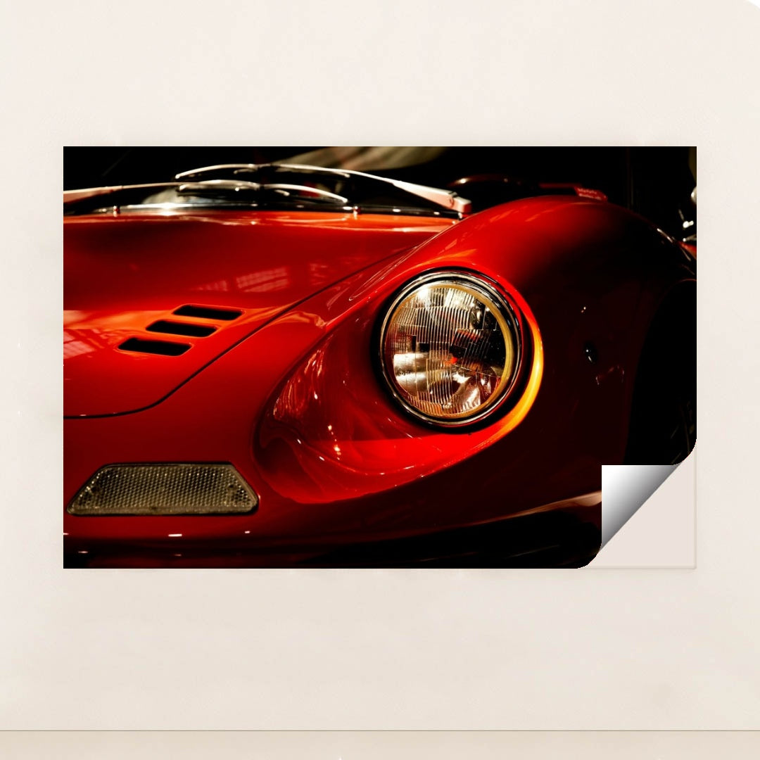This photo shows a close-up of the front left headlight and fender of a classic red Ferrari Dino, unframed style.