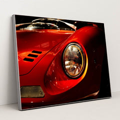 This photo shows a close-up of the front left headlight and fender of a classic red Ferrari Dino, in a silver frame.
