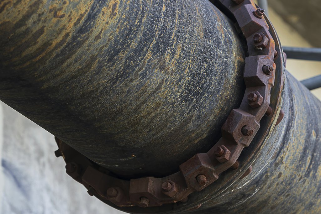 David Brown - Close-up of a rusty industrial pipe showing corrosion and bolted fittings.