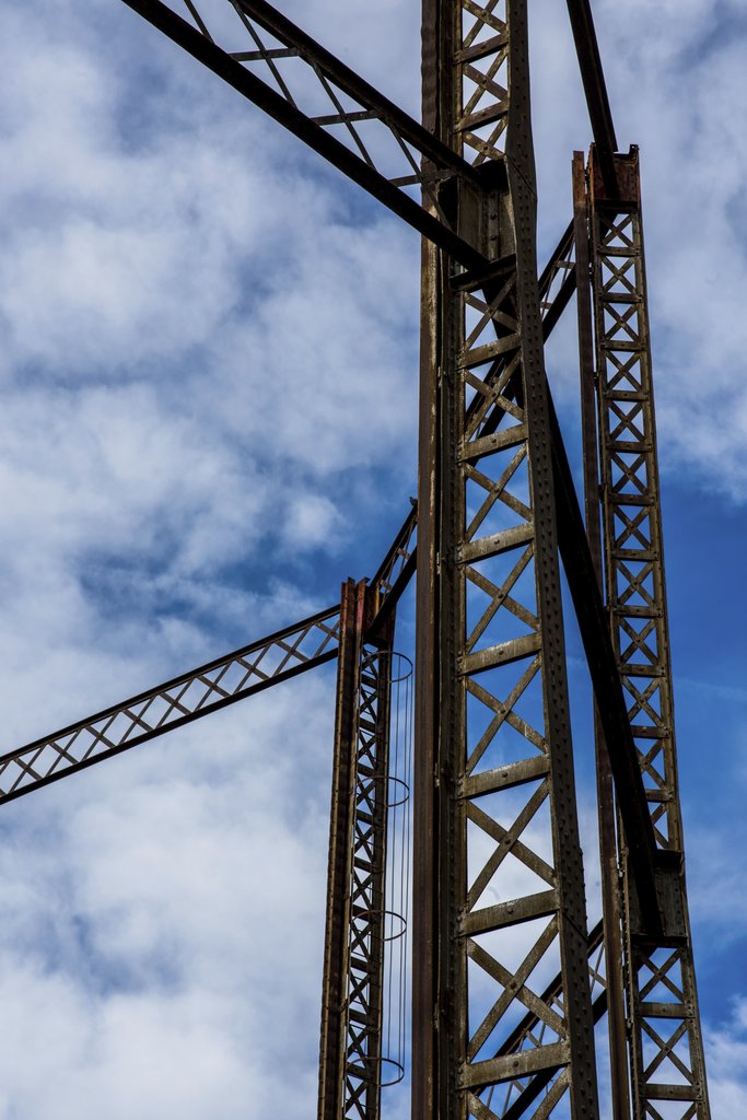 Victor Moragriega - A towering rusty industrial structure framed by a bright blue sky and scattered clouds.