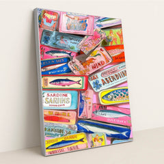 This artwork shows a colorful collection of decorative sardine cans with vintage-style labels, layered on a pink background, in a silver frame.