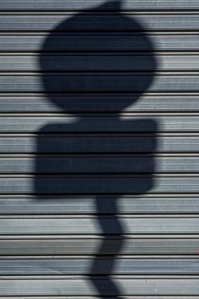 Victor Moragriega - Abstract shadow of a sign on a metal shutter, creating a dramatic visual contrast.