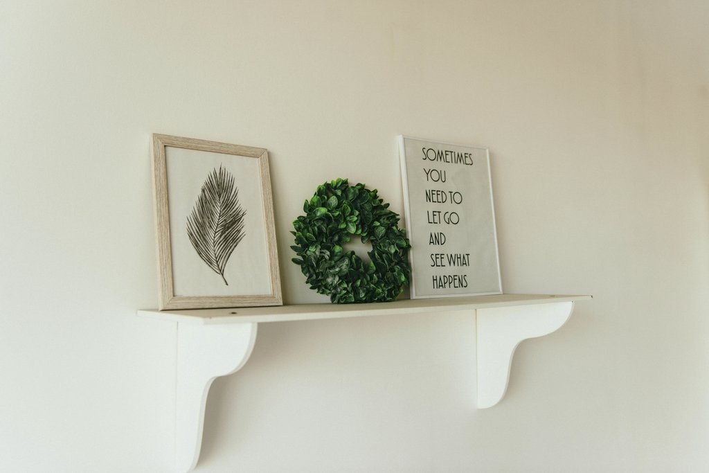 Dmitry Zvolskiy - A minimalist shelf with framed art, a green wreath, and an inspirational quote.