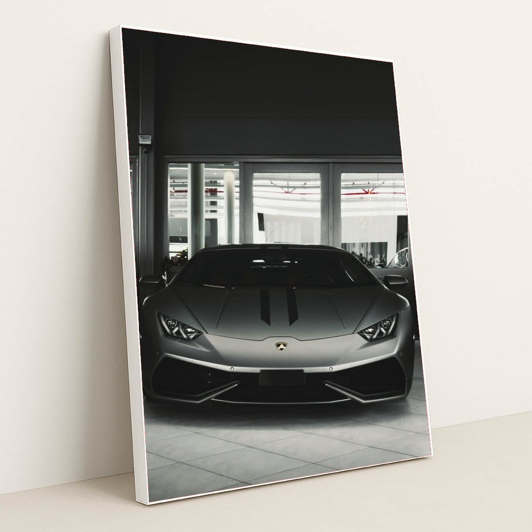 This photo shows the front view of a matte grey Lamborghini Huracán parked indoors, in a white frame.