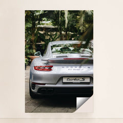This photo shows the rear view of a silver Porsche 911 Turbo S parked among lush green plants, minimalist unframed style.