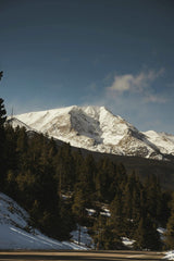 Jacob Moore - Beautiful winter scene of snow-covered Rocky Mountains and dense forested slopes under a clear blue sky.