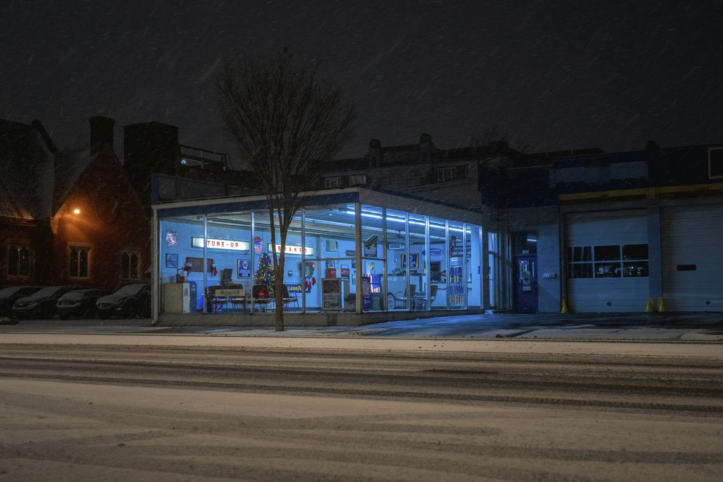 Mike Norris - Snowy night view of brightly lit gas station with neon lights and snow-covered street.