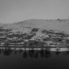 Sayefotograf - A serene winter landscape showing a snow-covered town by a river, reflecting a peaceful ambiance.