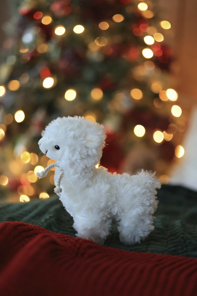 Valeria Boltneva - Adorable llama toy in front of a brightly lit Christmas tree, creating a festive holiday ambiance.