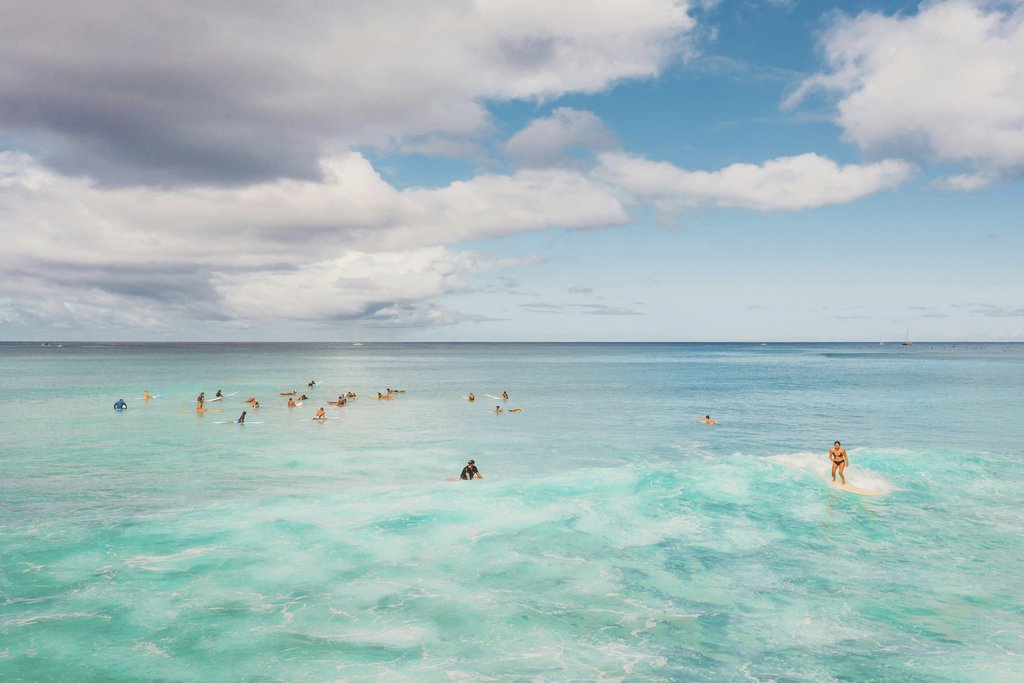 Jess Loiterton - Surfers riding waves under a vibrant sky in Hawaii, showcasing the island's adventurous spirit.