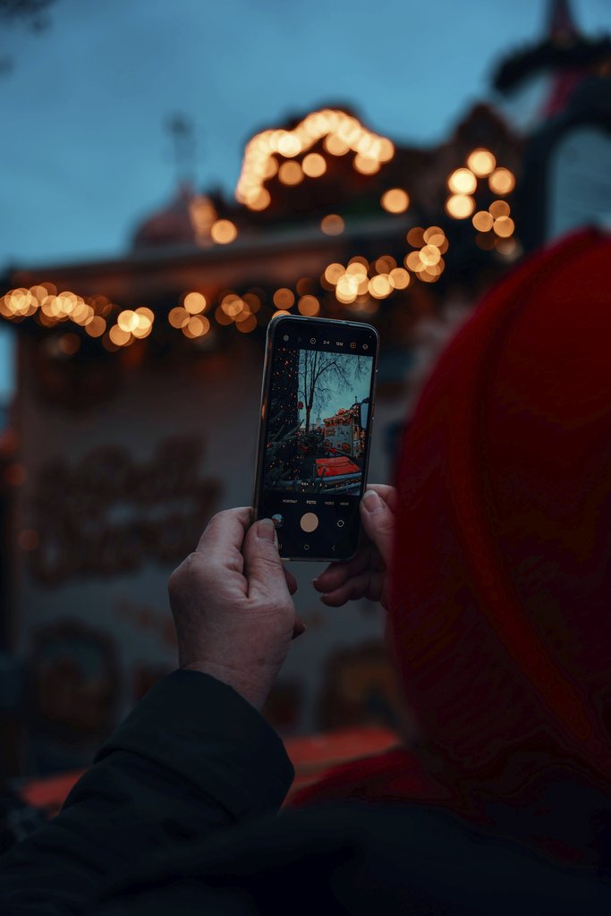Christiyana - A person photographing Berlin's Christmas market ambiance with a smartphone during the festive season.