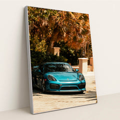 This photo shows a metallic blue Porsche sports car parked under tropical palm trees on a sunny day, in a silver frame.