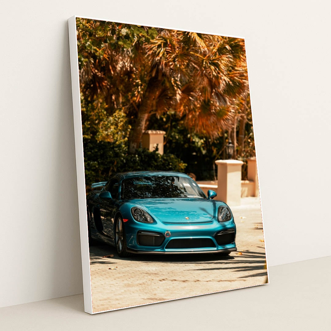 This photo shows a metallic blue Porsche sports car parked under tropical palm trees on a sunny day, in a white frame.