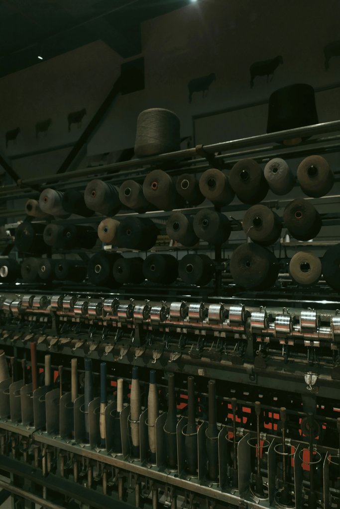 Melike Baran - Photo of old textile machine with spools indoors, dark industrial ambiance.