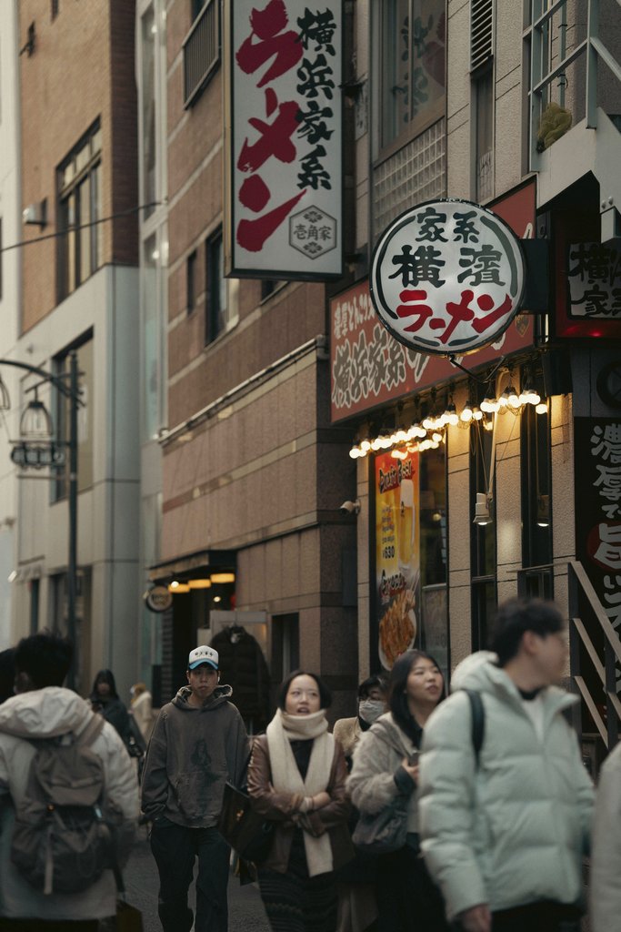Viridiana Rivera - A bustling street in Japan featuring vibrant signage and pedestrians walking past authentic ramen shops.