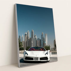 This photo shows a white Ferrari convertible with red seats parked in front of Dubai skyscrapers under a clear blue sky, in a silver frame.