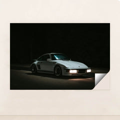 This photo shows a white Porsche 911 with pop-up headlights and wide body kit driving at night, minimalist unframed style.