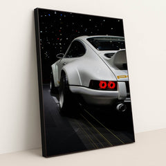 This photo shows the rear of a white Porsche sports car with a large wing, illuminated taillights, and starry reflections, in a black frame.