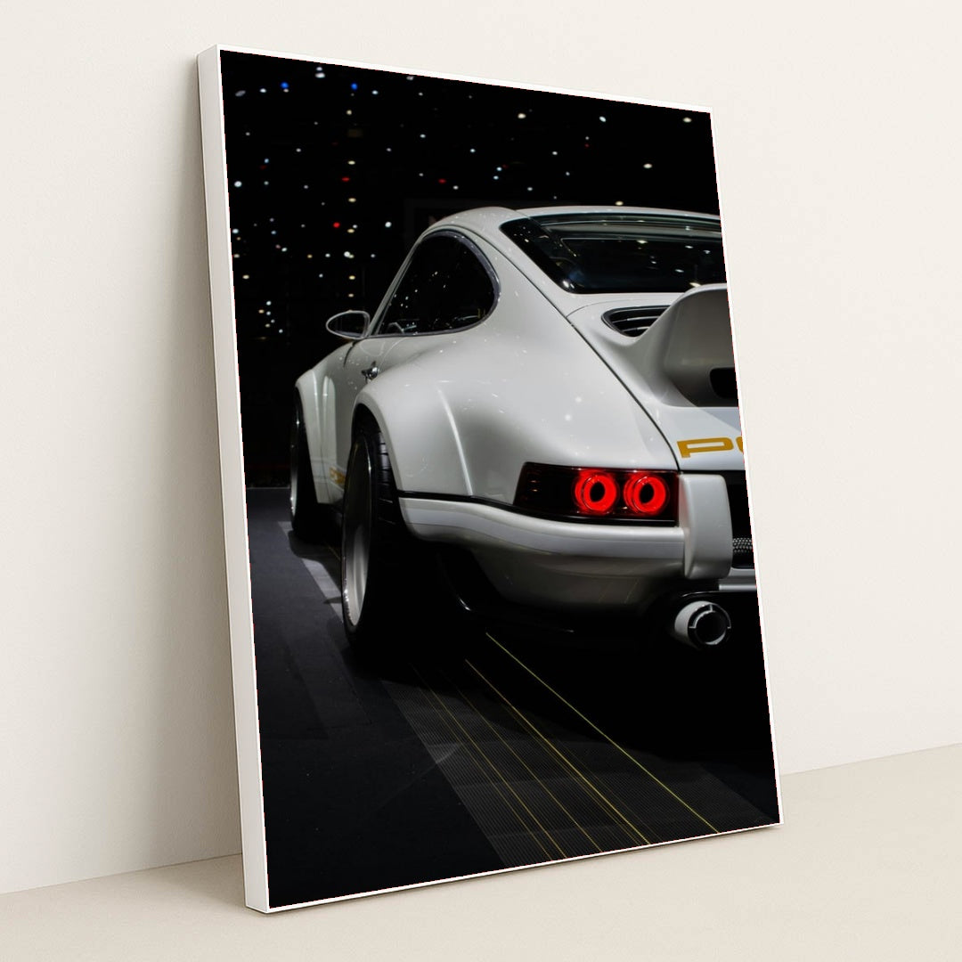 This photo shows the rear of a white Porsche sports car with a large wing, illuminated taillights, and starry reflections, in a white frame.