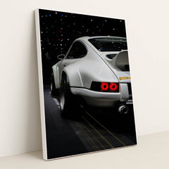 This photo shows the rear of a white Porsche sports car with a large wing, illuminated taillights, and starry reflections, in a white frame.