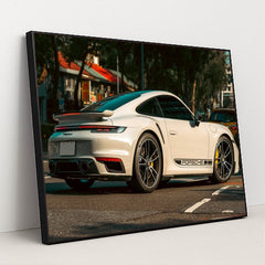 This photo shows a white Porsche 911 Turbo sports car parked on a street with black Porsche side decals, in a black frame.