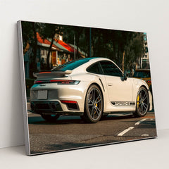 This photo shows a white Porsche 911 Turbo sports car parked on a street with black Porsche side decals, in a silver frame.