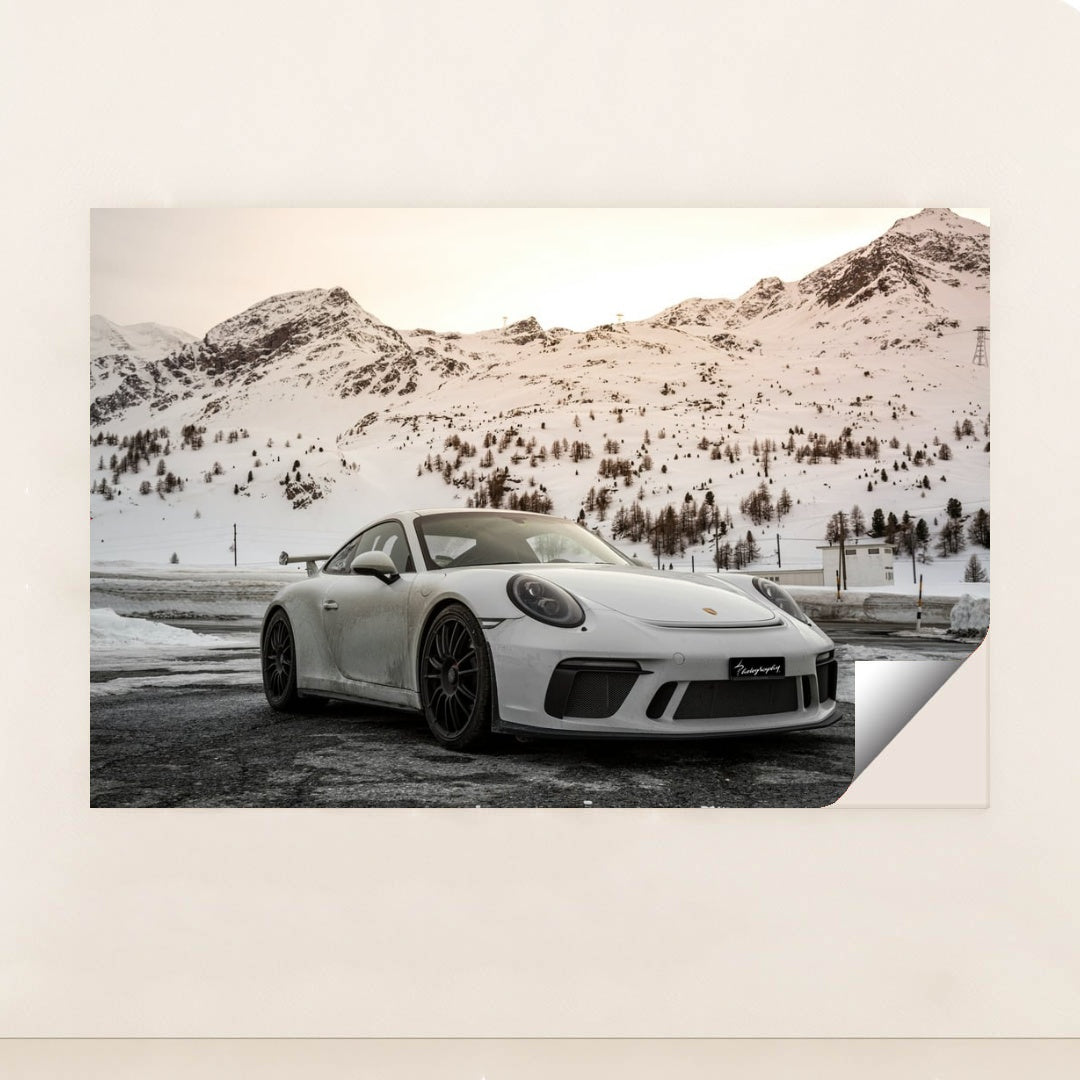 This photo shows a white Porsche sports car parked in front of snowy mountains at sunset, minimalist unframed style.