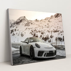 This photo shows a white Porsche sports car parked in front of snowy mountains at sunset, in a silver frame.