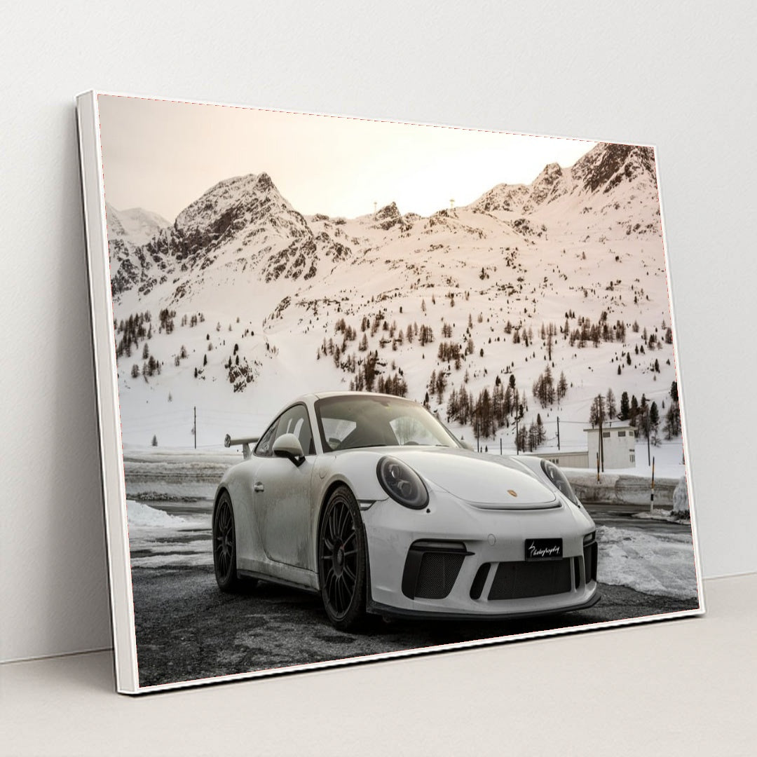 This photo shows a white Porsche sports car parked in front of snowy mountains at sunset, in a white frame.