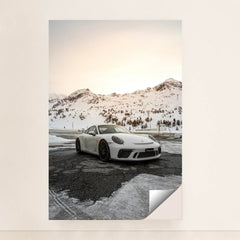 This photo shows a white Porsche sports car parked on a snow-covered mountain road at sunset, minimalist unframed style.